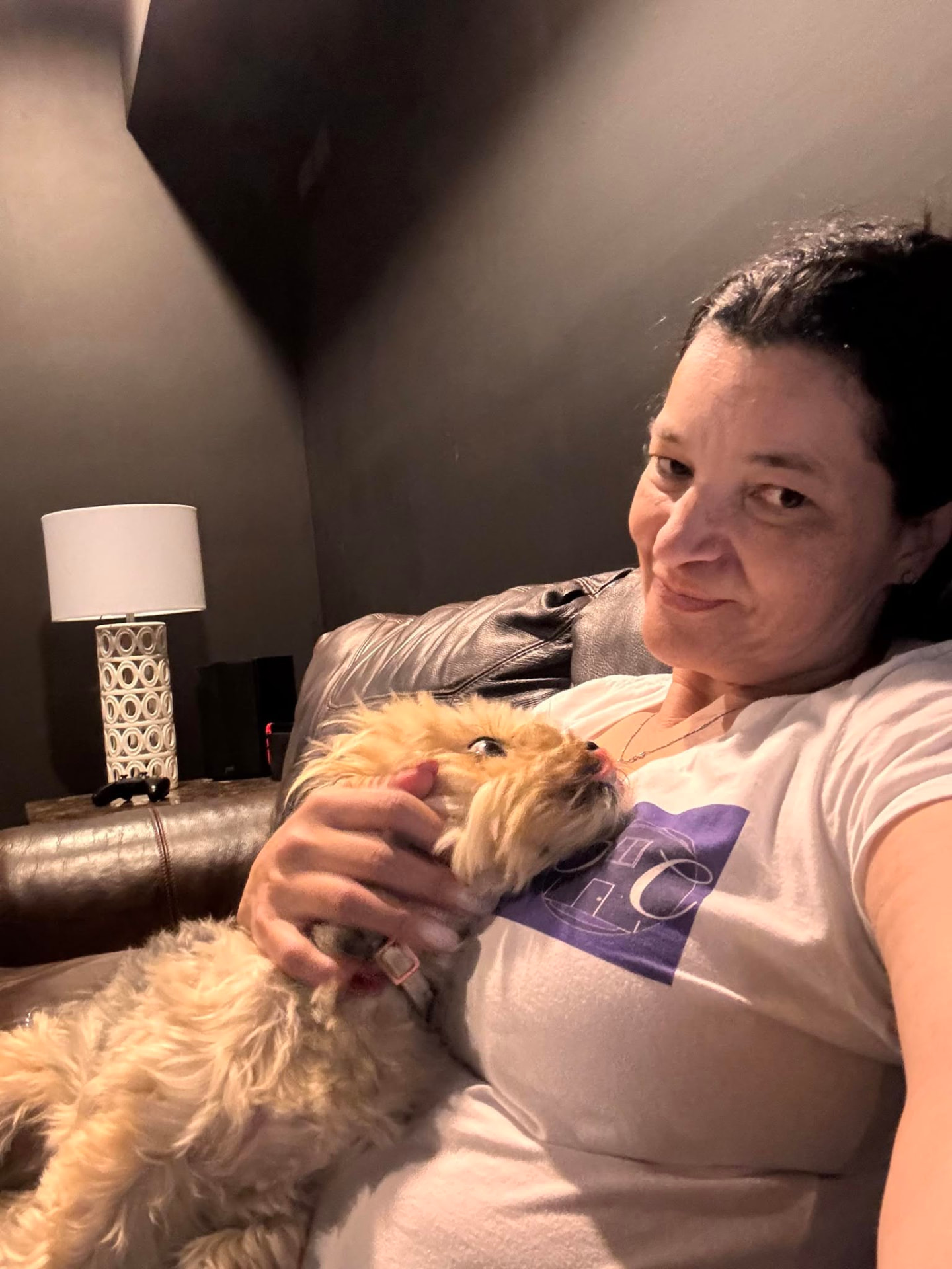 Small cream-colored dog cuddling in the arms of a Miles For Smiles caregiver on a sofa